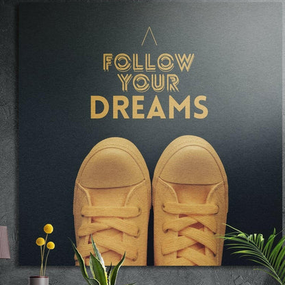 Yellow sneakers under gold motivational lettering on dark slate, brushed aluminum wall art on a concrete wall behind plants