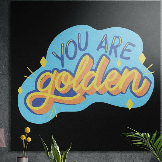 You are golden retro script on a sky blue cloud shape, brushed aluminum wall art on a dark wall behind plants