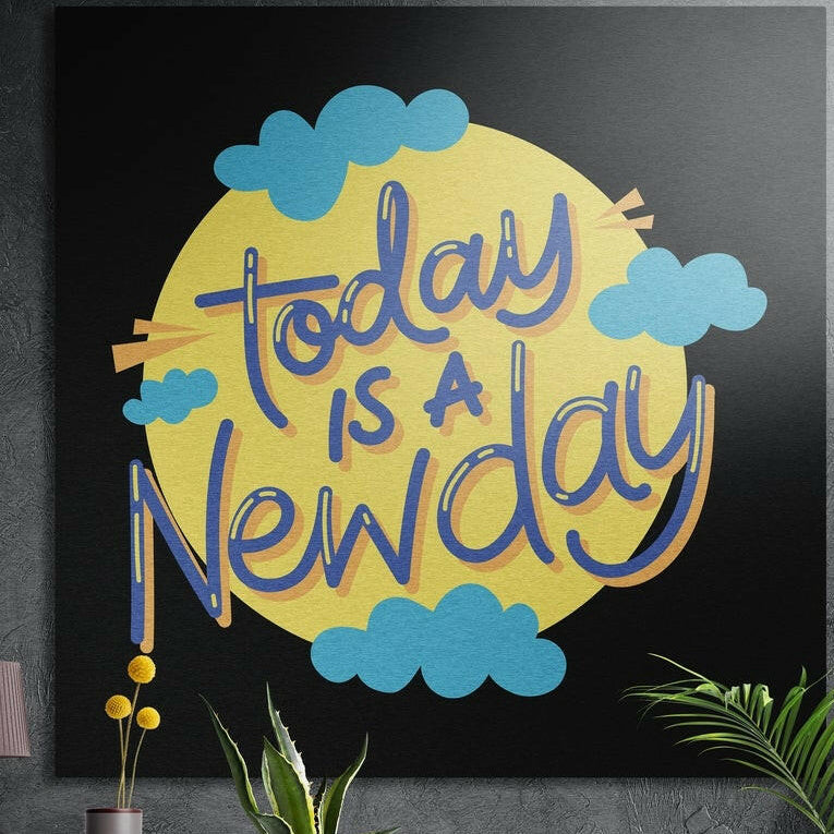 Today is a new day lettering on a yellow sun with blue clouds, brushed aluminum wall art on a dark wall behind plants