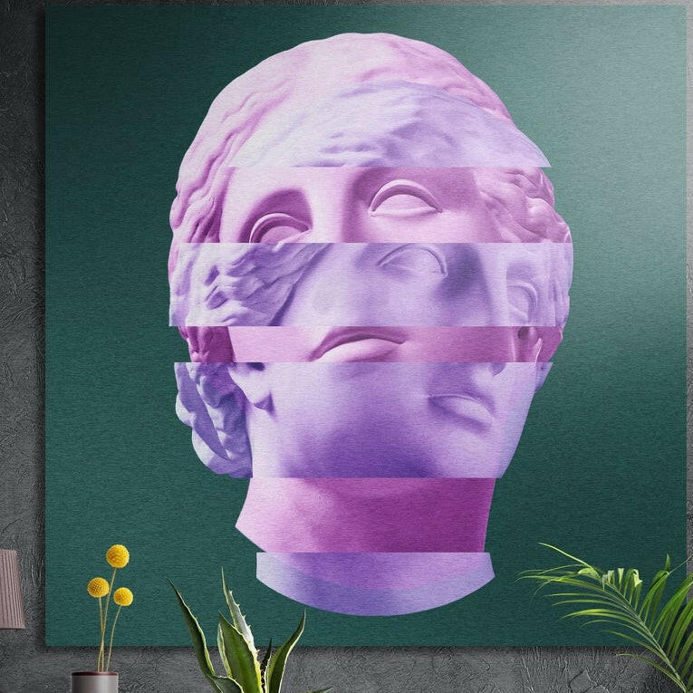 Pink and lilac sliced statue head brushed aluminum wall art on a gray wall above yellow flowers and plants