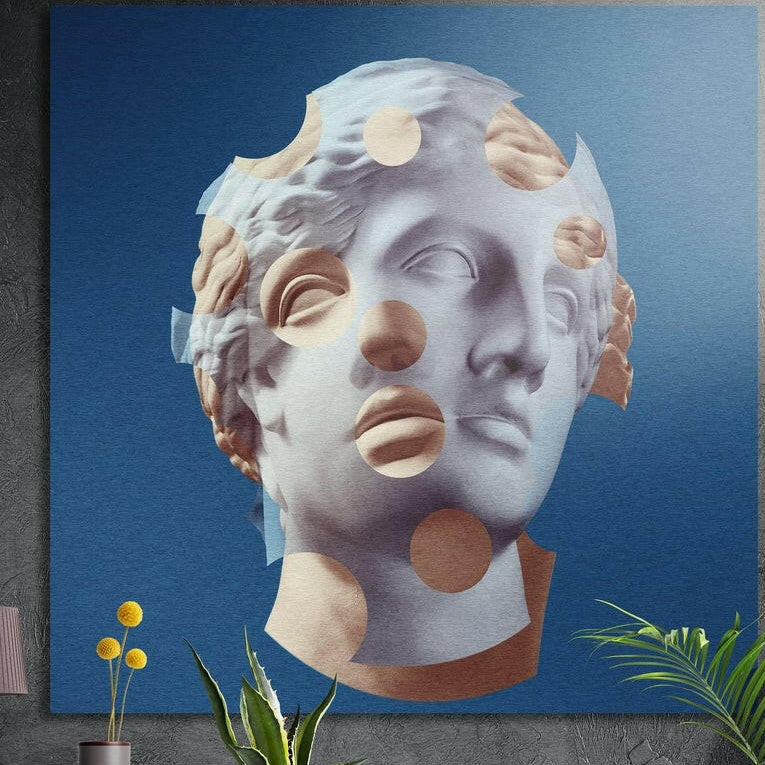 Blue statue head with tan cut-out circles brushed aluminum wall art on a gray wall above yellow flowers and plants