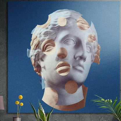 Blue statue head with tan cut-out circles brushed aluminum wall art on a gray wall above yellow flowers and plants