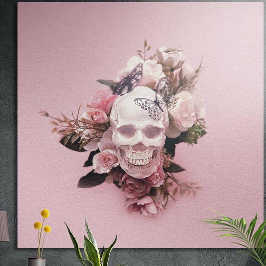 Blush pink rose and butterfly skull brushed aluminum wall art on a dark concrete wall behind potted plants