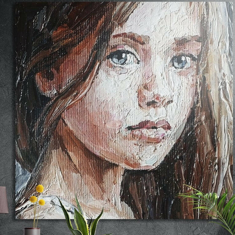 Painted brown-haired girl portrait brushed aluminum wall art on a dark concrete wall above yellow flowers and plants