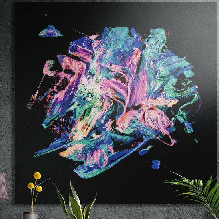 Pink and teal paint burst brushed aluminum wall art on black, square, on a dark wall behind potted plants