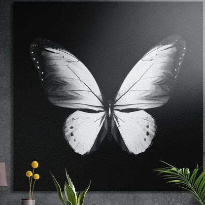 White butterfly brushed aluminum wall art on a dark concrete wall above a vase and plants
