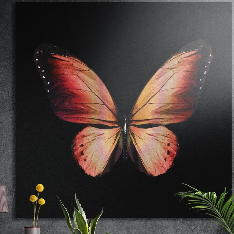 Coral orange butterfly on black brushed aluminum wall art on a dark wall behind a vase of yellow flowers and plants