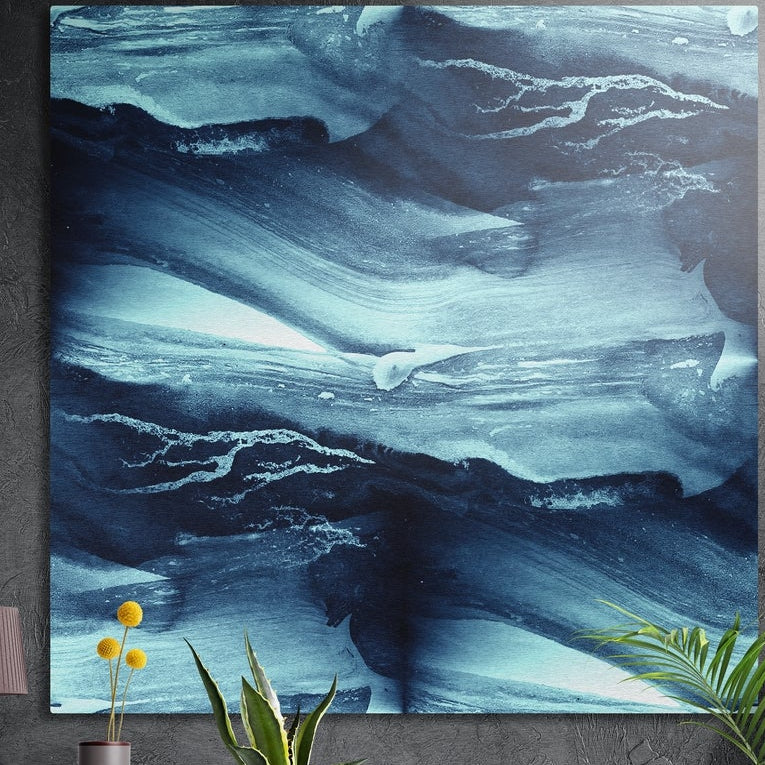 Deep indigo marbled ink waves brushed aluminum wall art on a dark wall behind a vase of yellow flowers and plants