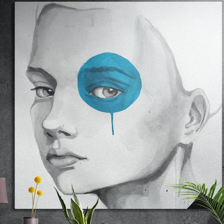 Gray sketch of a woman's face with one eye in a blue blot, square brushed aluminum wall art on a dark wall above leaves