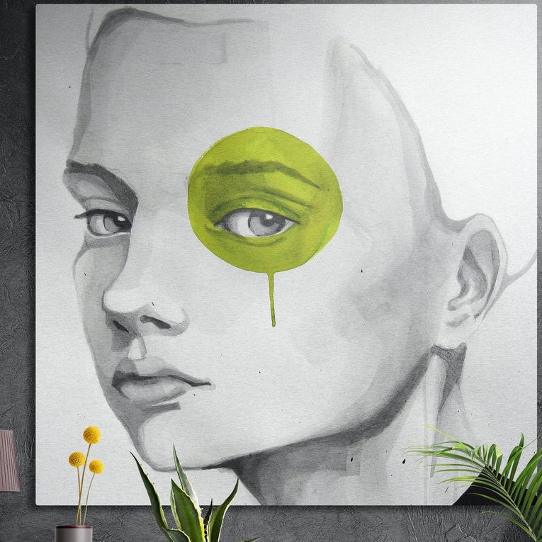 Gray sketch of a woman with one eye in a lime green blot, square brushed aluminum wall art on a dark wall with leaves below
