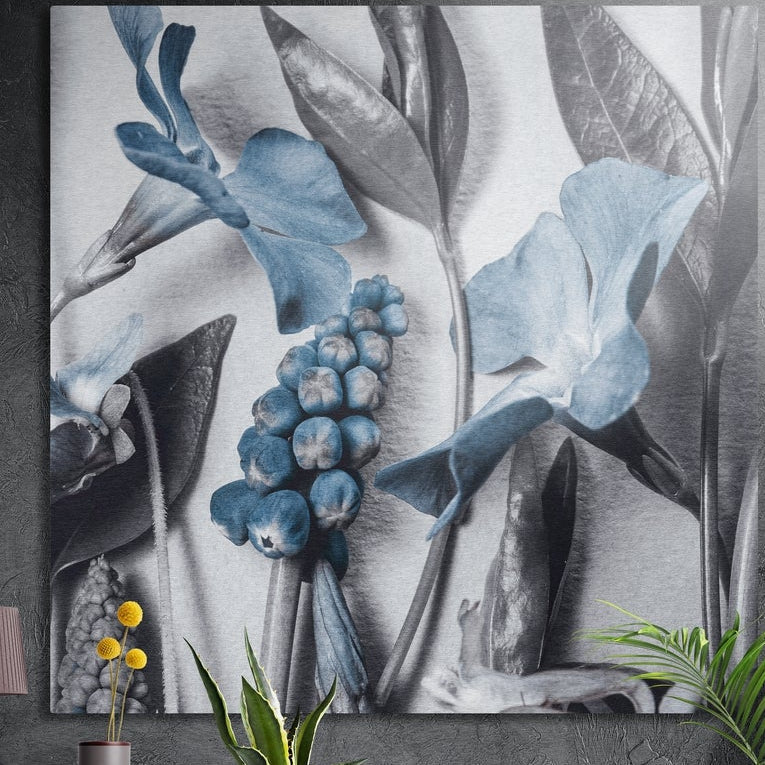 Blue blossoms and blue berries among silver-gray leaves, brushed aluminum wall art on a concrete wall behind plants