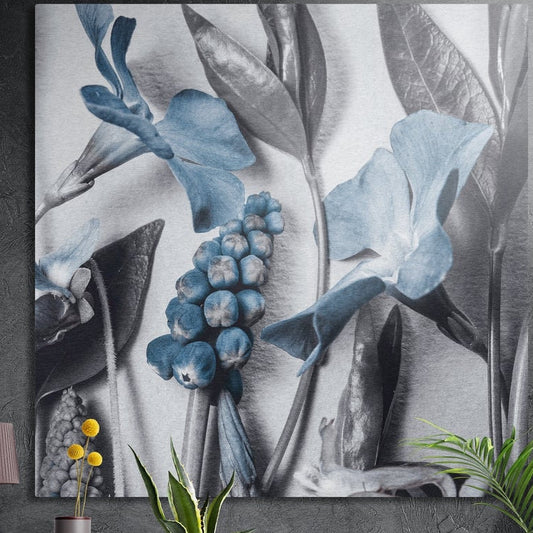 Blue blossoms and blue berries among silver-gray leaves, brushed aluminum wall art on a concrete wall behind plants