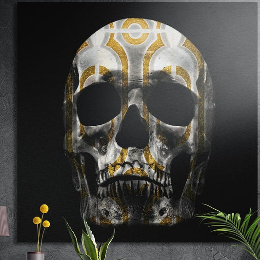 Gold patterned silver skull square brushed aluminum wall art on a gray concrete wall with plants in front