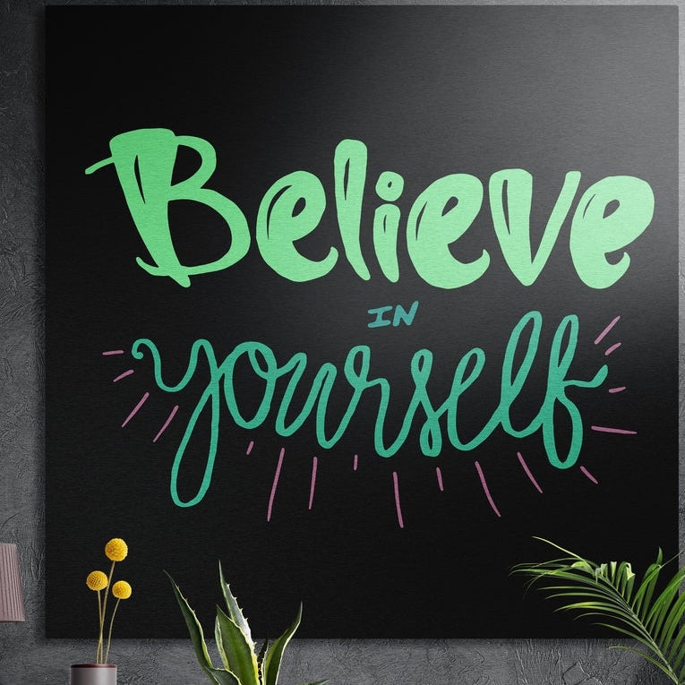 Believe in yourself green script brushed aluminum wall art on a dark textured wall above potted plants
