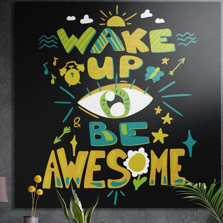 Wake Up Be Awesome lettering around a green eye on black, brushed aluminum wall art on a concrete wall behind plants