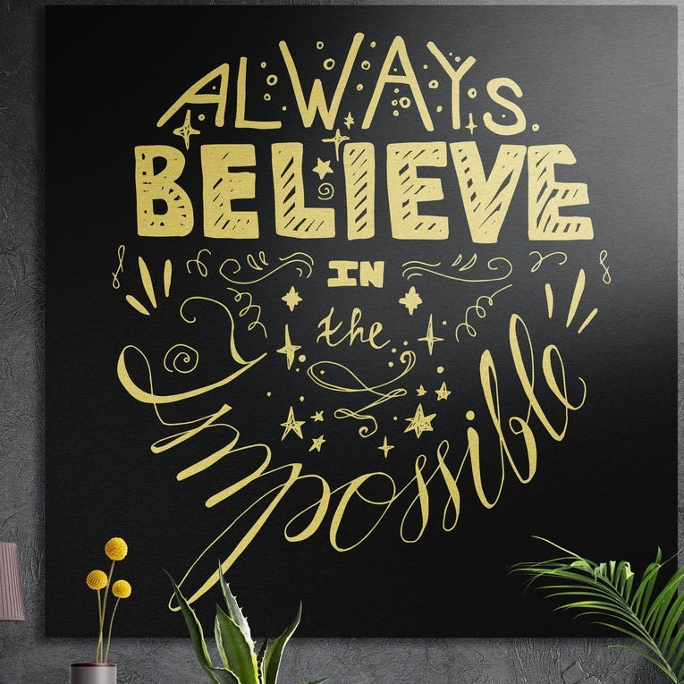 Always believe gold hand lettering brushed aluminum wall art on a dark textured wall above potted plants