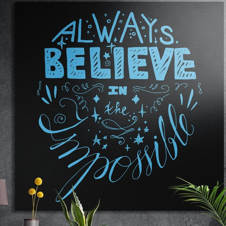 Always believe sky blue hand lettering brushed aluminum wall art on a dark textured wall above potted plants