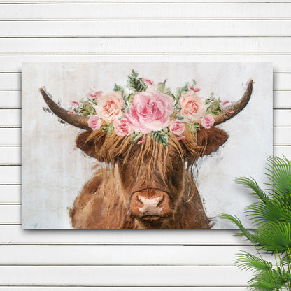 Canvas of a brown Highland cow wearing a pink rose flower crown, on a white shiplap wall beside a palm leaf