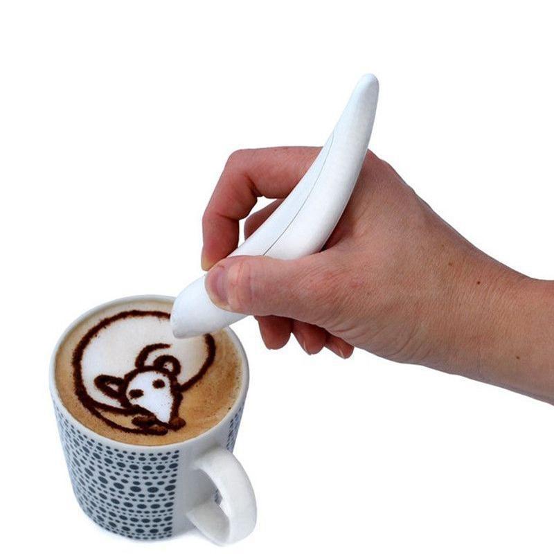 A hand using a white latte art pen to draw a design on the surface of a coffee drink in a cup.