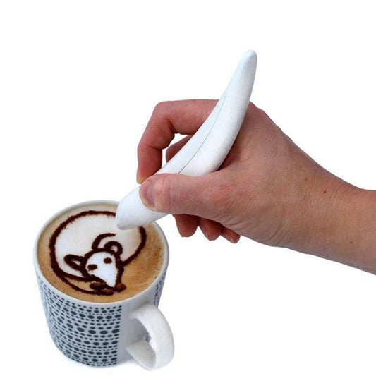 A hand using a white latte art pen to draw a design on the surface of a coffee drink in a cup.