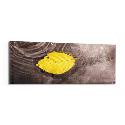 Yellow leaf on rippled water panoramic glass wall art shown on a white background with a soft shadow