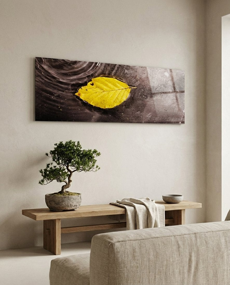Yellow leaf floating on dark rippled water, panoramic glass wall art above a bonsai tree on a low wooden bench