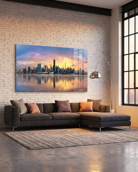Manhattan skyline at sunset mirrored in the river, panoramic glass wall art above a sectional sofa by a brick wall