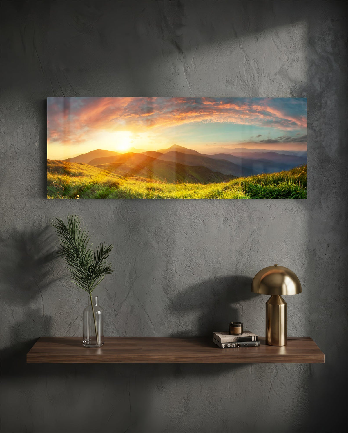 Golden sunset green hills panoramic glass wall art above a wood shelf with a brass lamp on a dark wall
