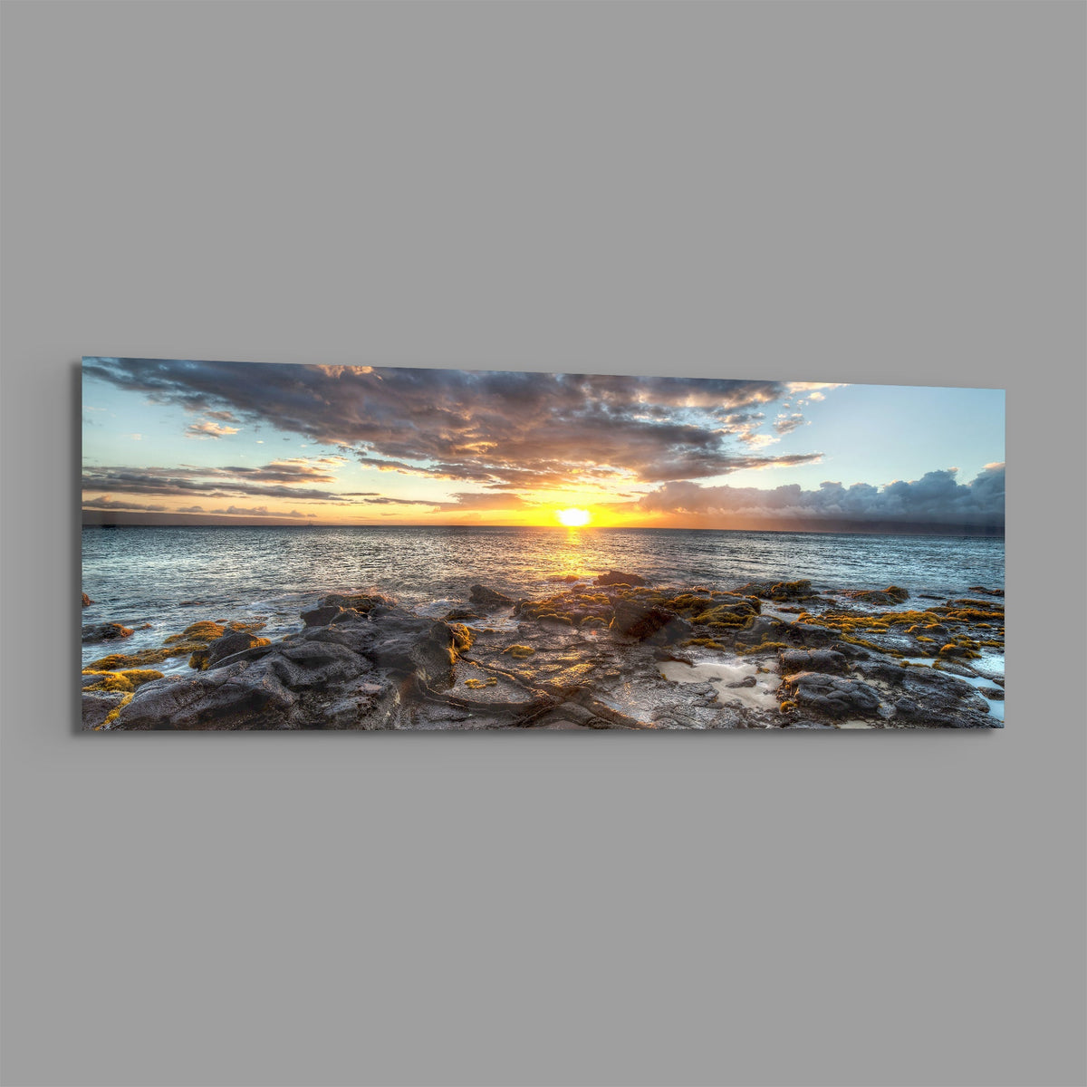Rocky shore ocean sunset panoramic glass wall art on a plain gray wall