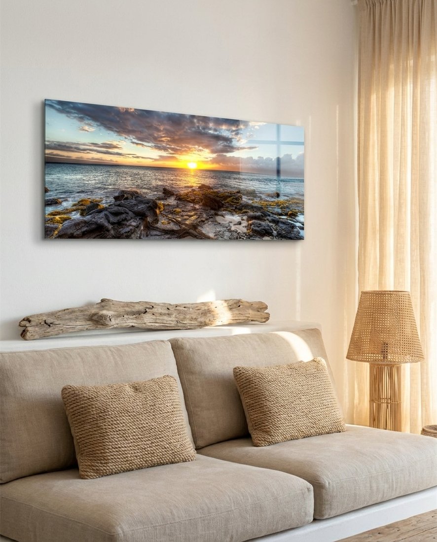 Rocky shore ocean sunset panoramic glass wall art above a beige sofa with driftwood and a rattan lamp