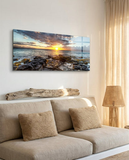 Rocky shore ocean sunset panoramic glass wall art above a beige sofa with driftwood and a rattan lamp