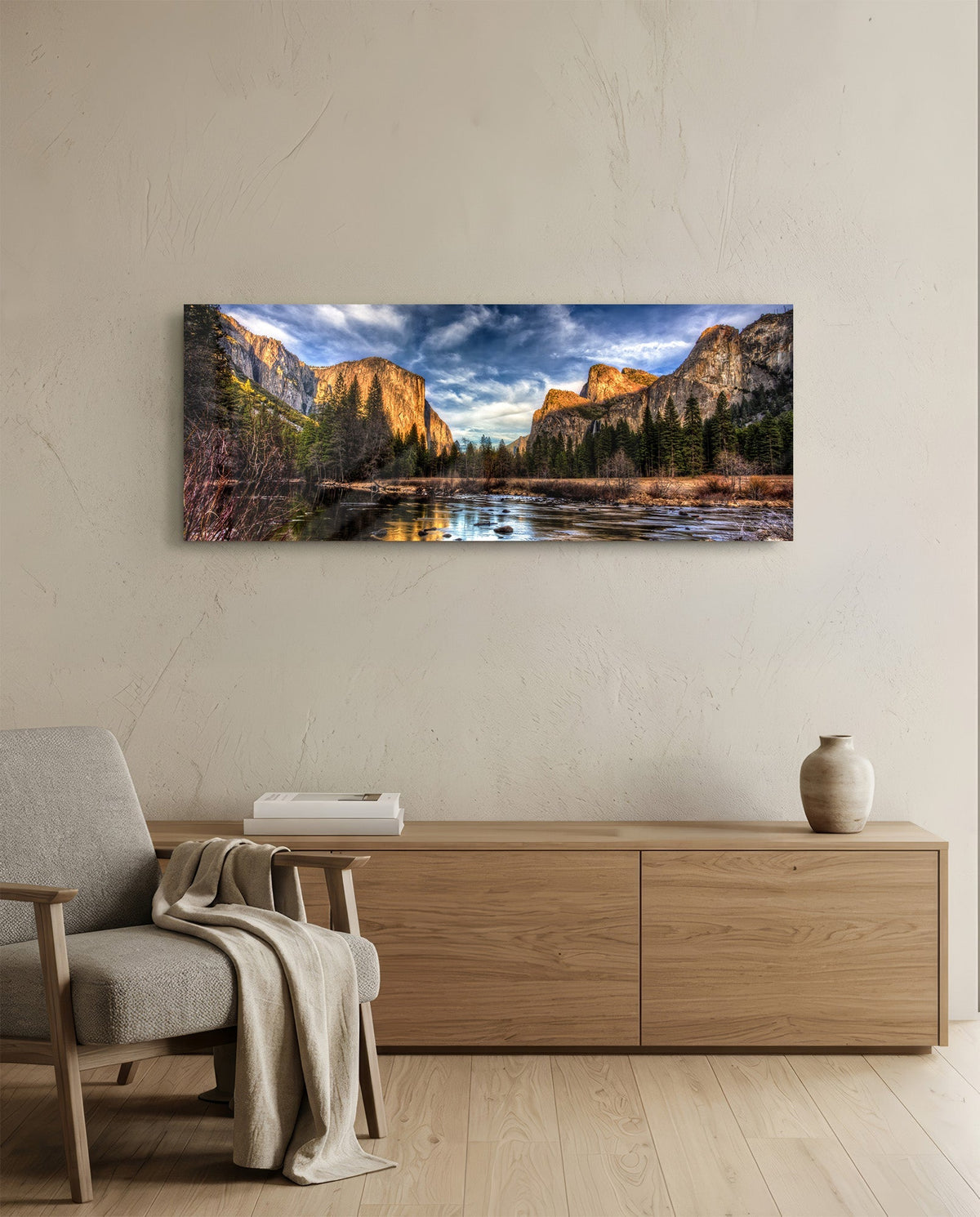 Granite cliffs river valley panoramic glass wall art above a light wood sideboard beside a gray armchair