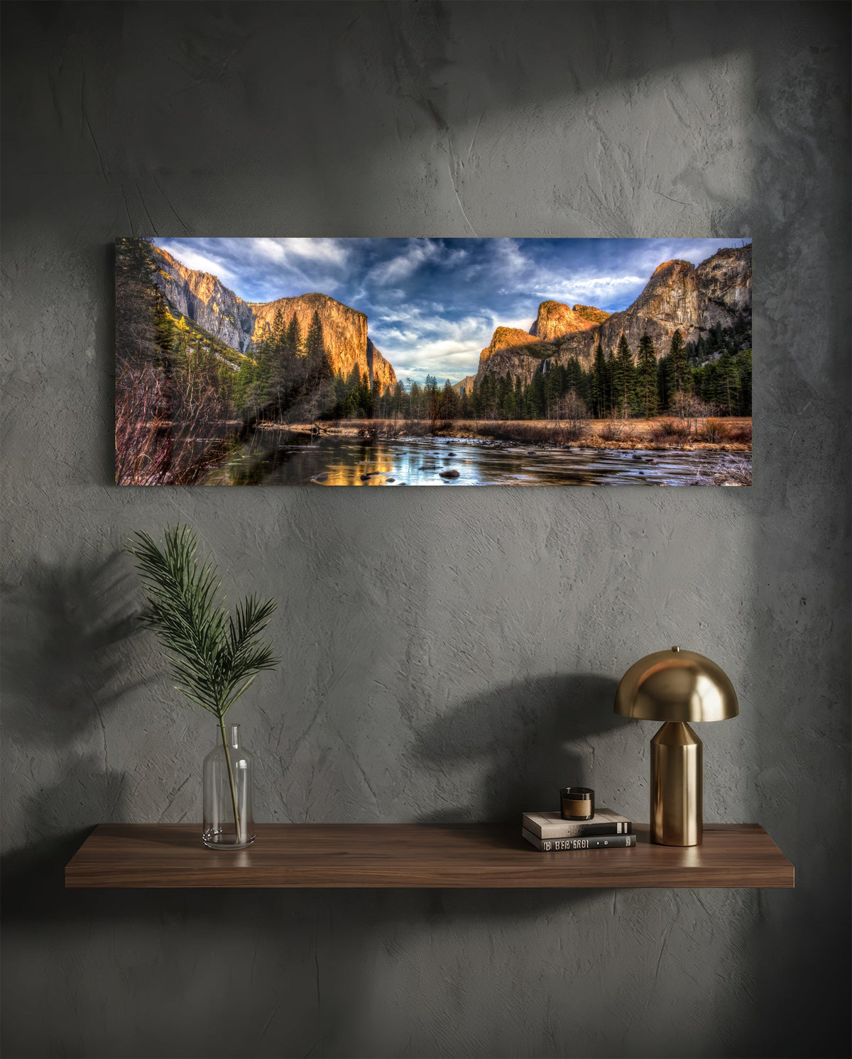 Granite cliffs river valley panoramic glass wall art above a wood shelf with a brass lamp on a dark wall
