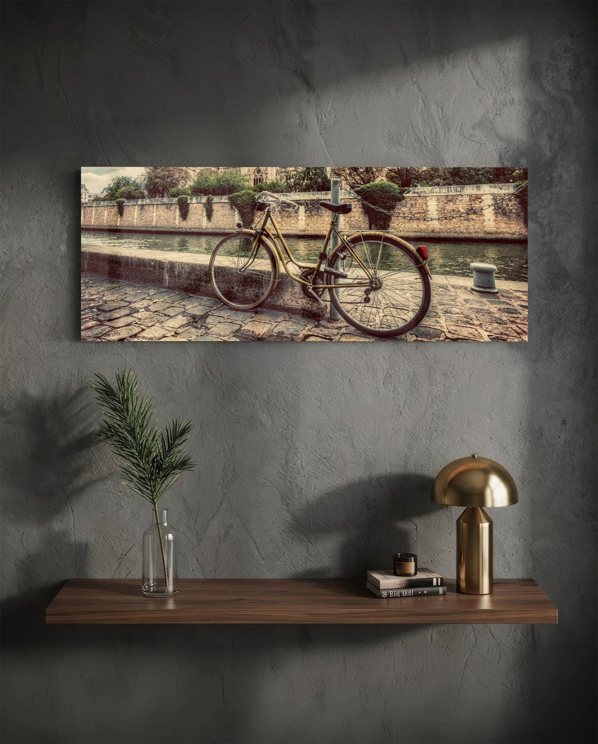 Vintage riverside bicycle glass wall art on a charcoal wall above a floating shelf with a brass lamp and greenery