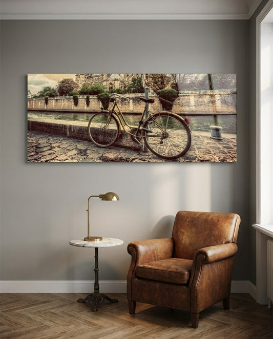 Vintage bicycle glass wall art above a brown leather armchair and a brass reading lamp on a gray wall
