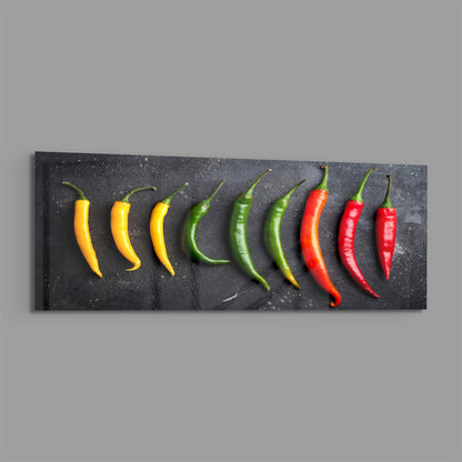 Chili peppers on black slate panoramic glass piece shown on a plain gray background