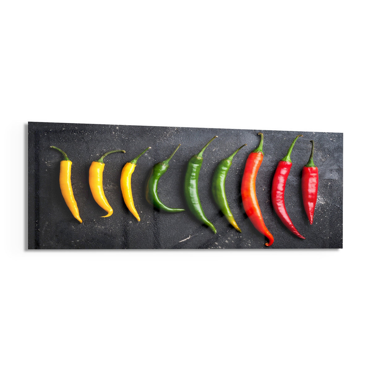 Chili peppers on black slate panoramic glass piece shown on a white background