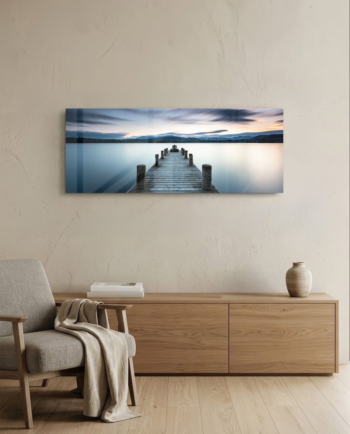 Blue hour lake jetty glass wall art above a light oak sideboard beside a cream armchair