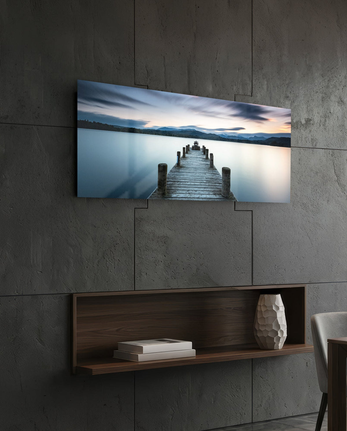 Blue hour lake jetty glass wall art above a dark wood wall shelf on a charcoal paneled wall