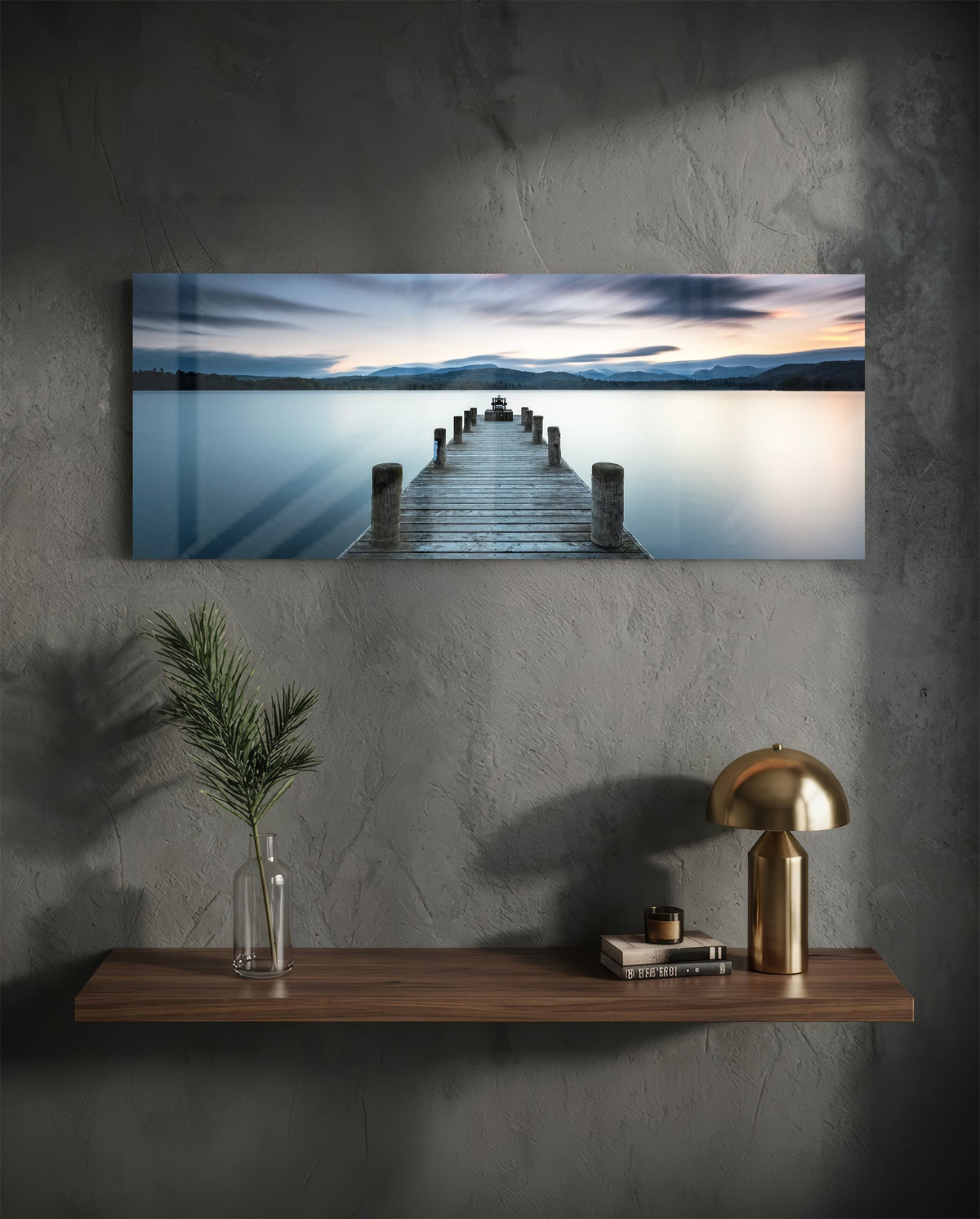 Blue hour lake jetty glass wall art above a floating walnut shelf with a brass lamp