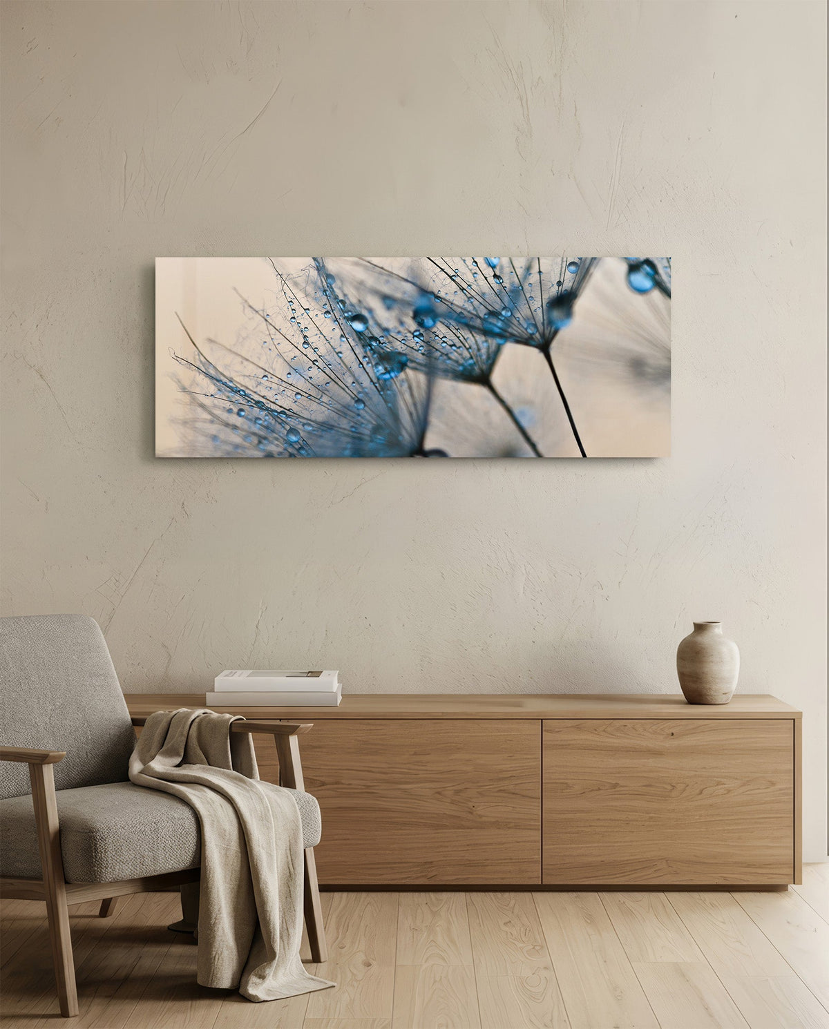 Blue dandelion panoramic glass wall art above a low wood sideboard and a gray armchair with a throw