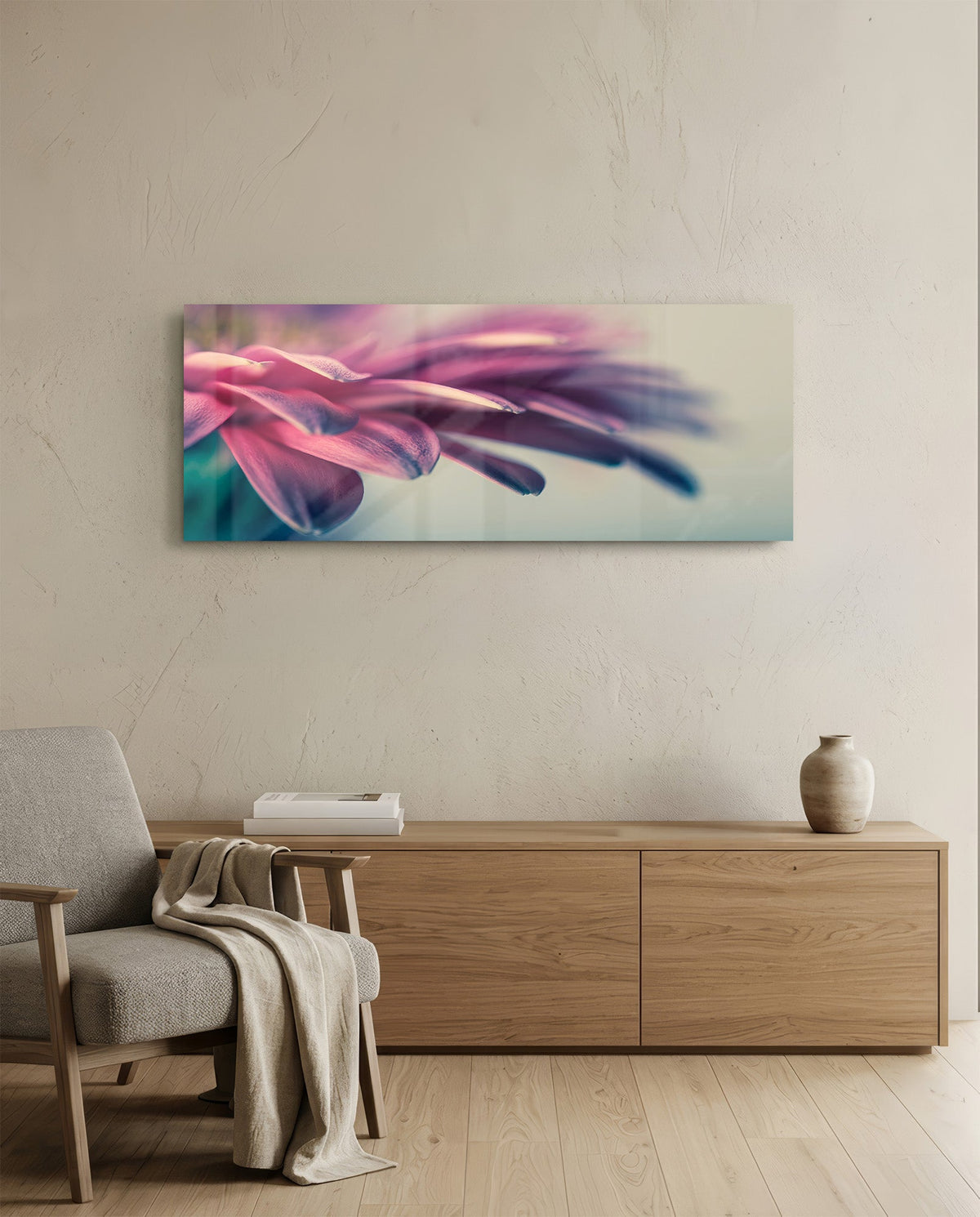 Pink flower petal macro glass wall art above a light wood sideboard beside a gray armchair with a throw