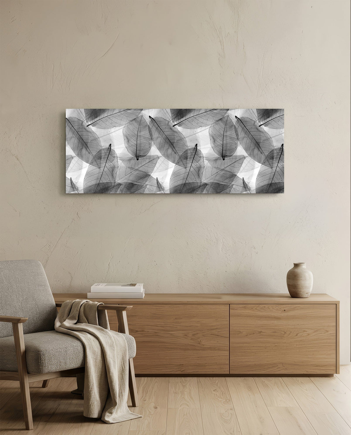 Black and white skeleton leaves glass wall art above an oak sideboard beside a wooden armchair with a throw