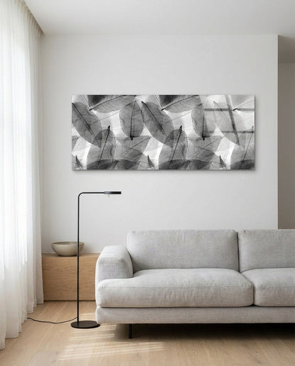 Black and white skeleton leaves with fine veins in soft gray layers, panoramic glass wall art above a light gray sofa