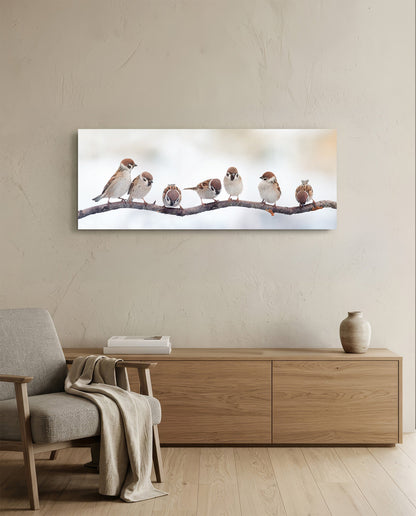 Sparrows on a branch glass wall art above a low wood sideboard beside a gray armchair