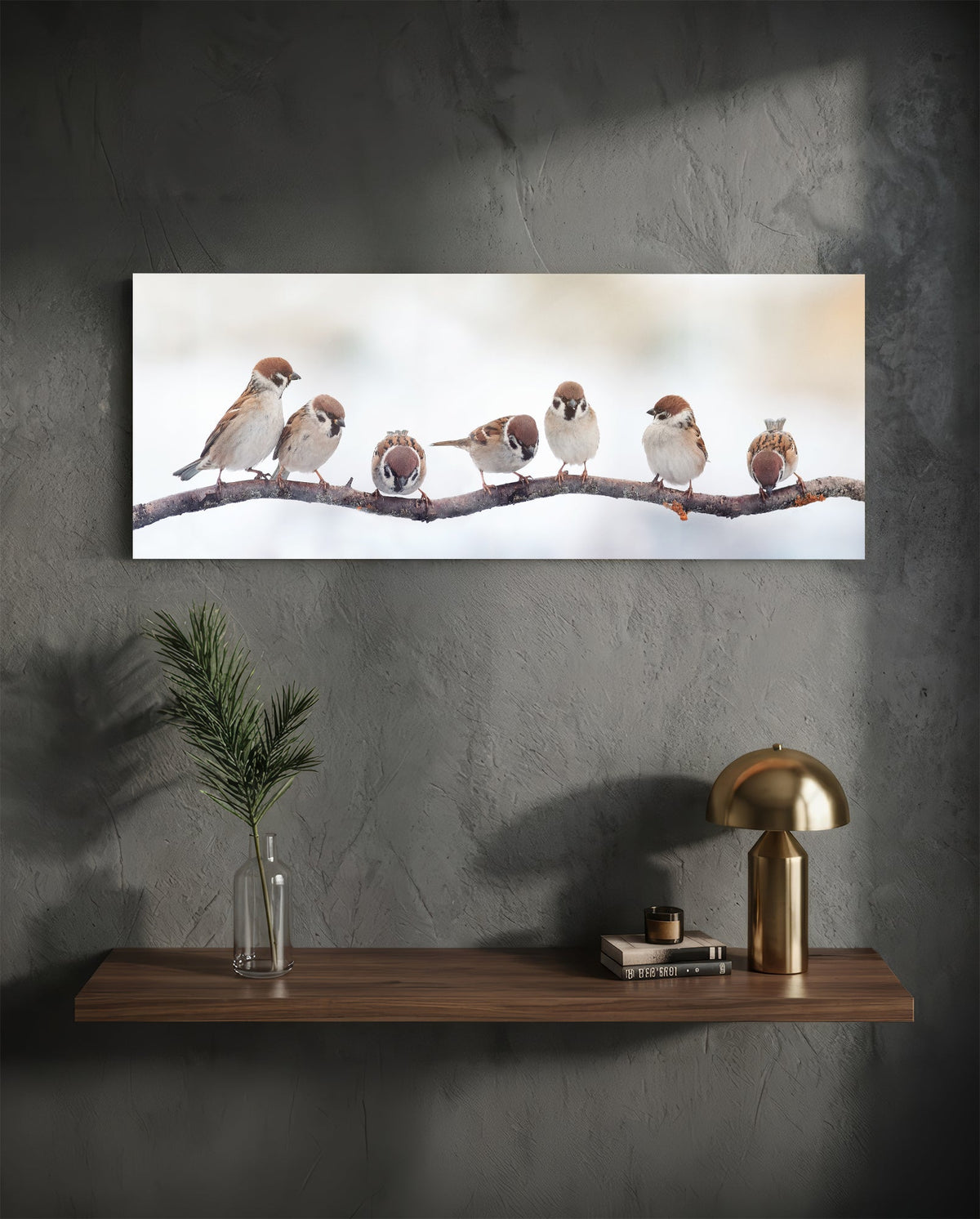 Sparrows on a bare branch glass wall art on a dark plaster wall above a floating shelf with a brass lamp