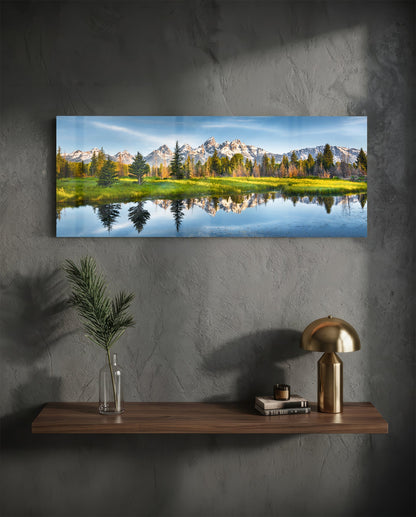 Mountain lake reflection glass wall art on a charcoal wall above a floating shelf with a brass lamp and greenery