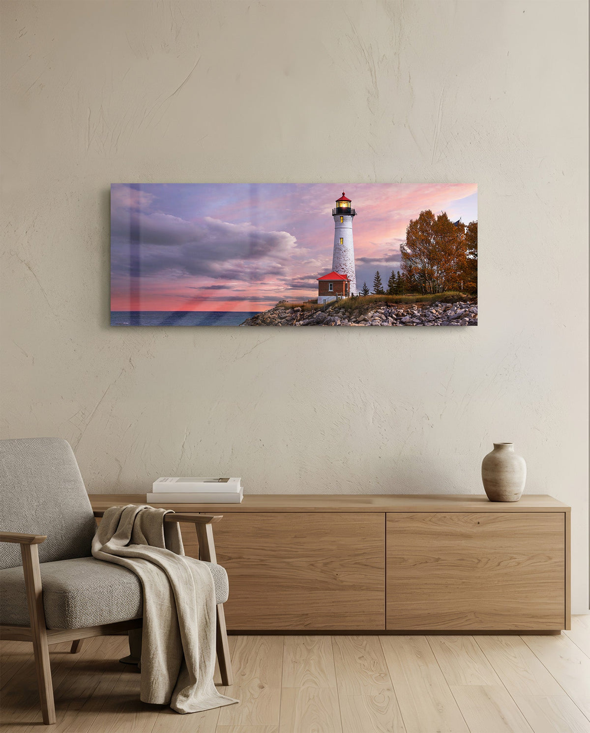 Lighthouse at dusk glass wall art above a light oak sideboard beside a cream armchair