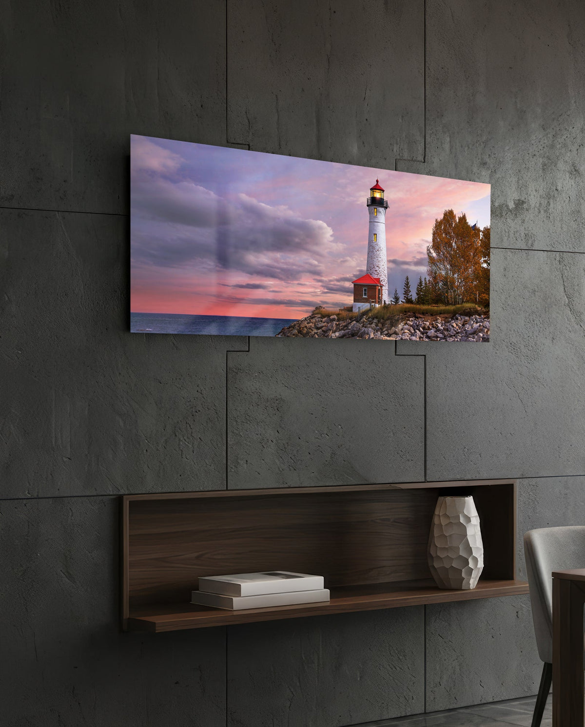 Lighthouse at dusk glass wall art above a dark wood wall shelf on a charcoal paneled wall