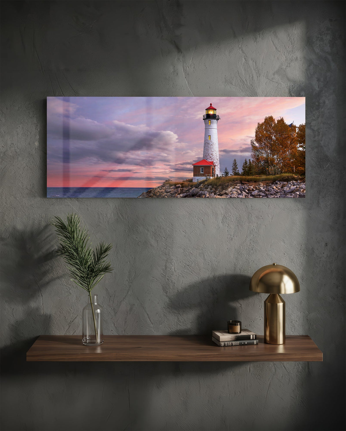 Lighthouse at dusk glass wall art above a floating walnut shelf with a brass lamp